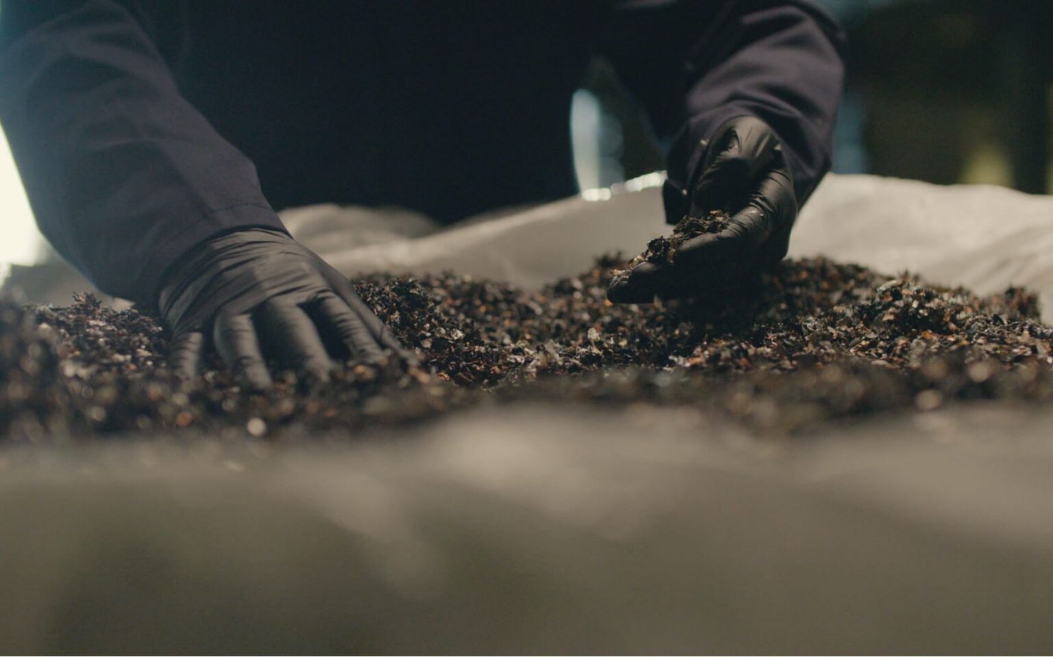 gloved hands sifting through recycled lithium elements